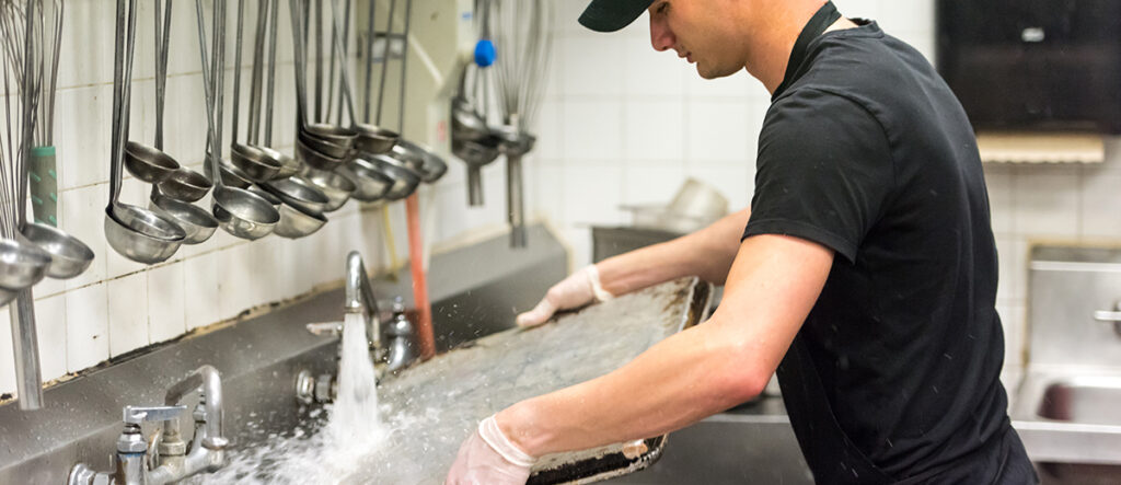 A photo of a person washing a large pan in an industrial sink