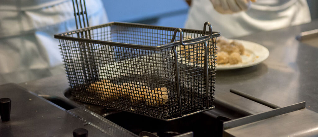 A photo of a restaurant employee using a deep fryer